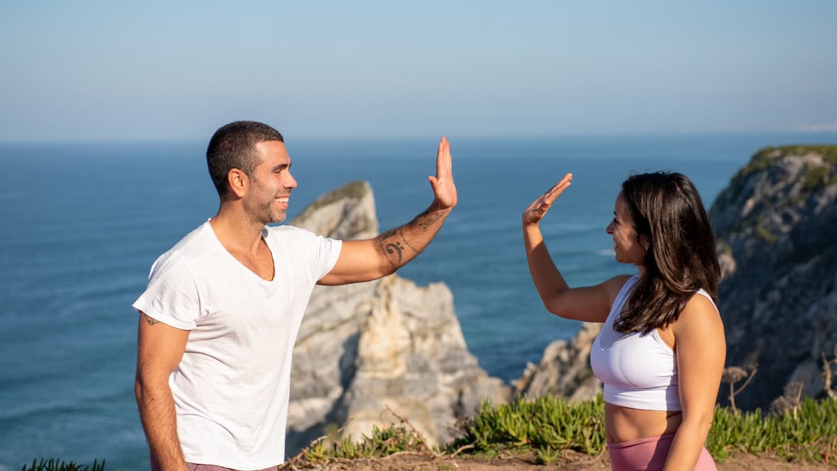 Fit couple in athletic wear high-fiving by the sea on a sunny day in Portugal.